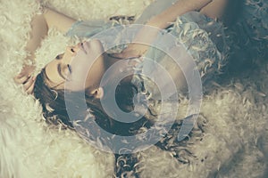 Sleeping beauty. Cute girl relaxing on feather bed pillow and mattress. Pretty girl in silky pajamas with feather in