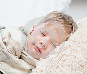 Sleeping boy lying in bed with a thermometer in mouth