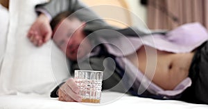Sleeping businessman sleeps in bed in a hotel room and holds alcohol