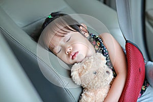 Sleeping child in car seat belt hugging teddy bear