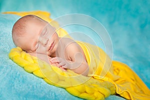 Sleeping cute newborn baby on a yellow chunky knit blanket