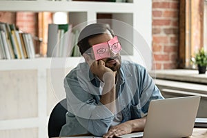 Sleeping employee hides eyes under sticky notes seated at desk