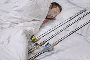 Sleeping fisherman in bed with fishing tackles. Think and dream about big fish trophy