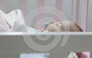 Sleeping four month baby boy lying in cot with pacifier