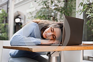 Sleeping girl with laptop on the table outdoor in cafe. Tired young woman have a break at work and sleeping and relaxing