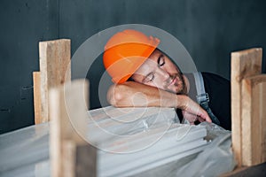 Sleeping on a job. Taking a break. Industrial worker indoors in factory. Young technician with orange hard hat