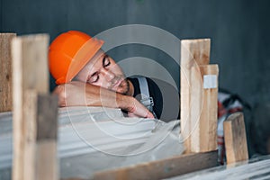 Sleeping on a job. Taking a break. Industrial worker indoors in factory. Young technician with orange hard hat