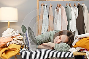 Sleeping lazy brown haired woman wearing knitted shirt ironing clothing while sitting in her wardrobe sleeping on ironing board