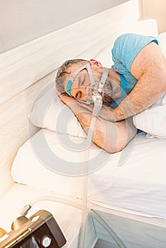 Sleeping man with chronic breathing issues considers using CPAP machine in bed.