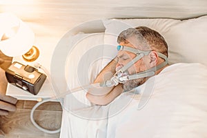 Sleeping man with chronic breathing issues considers using CPAP machine in bed.