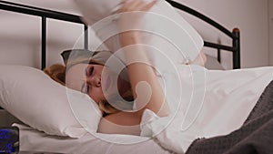 Sleeping middle aged woman disturbed by noise covering head with pillow in bed