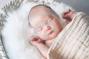 Sleeping newborn baby in basket wrapped in blanket in white fur background. Portrait of little child one week old