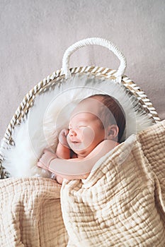 Sleeping newborn baby in basket wrapped in blanket in white fur background. Portrait of little child one week old