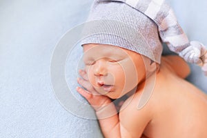 Sleeping newborn baby on the blue background. Child in a nightcap close-up portrait