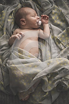 Sleeping newborn baby laying on the bed wrapped in the scarf