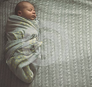 Sleeping newborn baby laying on the bed wrapped in the scarf