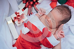 Sleeping newborn baby on mother hand in Christmas hat with gift