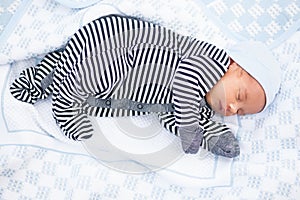 Sleeping newborn baby in striped romper on coverlet.