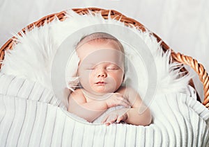 Sleeping newborn baby in a wrap on white blanket.