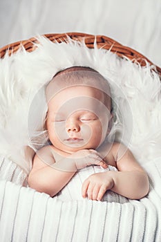 Sleeping newborn baby in a wrap on white blanket.