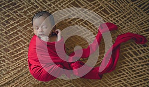 Sleeping peacefully newborn baby boy wrapped in red cloth, 1 month old baby lying on latticework. photo