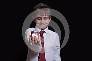 Sleeping schoolboy with a red alarm clock in his hands. Morning concept. Black background. Isolate