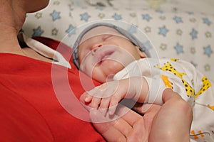 Sleeping smiling happy newborn babe holding hands with father close up