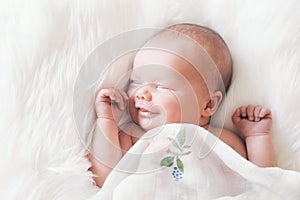 Sleeping smiling newborn baby in a wrap on white blanket.