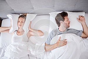 Sleeping, snoring and wife with pillow on ears to stop noise from husband in bed with sleep problem. Insomnia