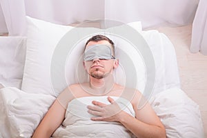 Sleeping young man in sleep mask on bed.