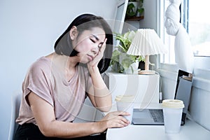 Asian woman feeling tired and fall asleep at home office with laptop and cup of coffee photo