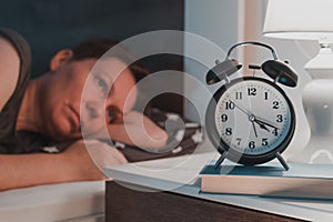 Sleepless insomniac woman lying in bed and looking at alarm clock on bedside nightstand