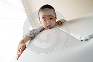 Sleepy Asian baby boy climbing playpen to looking after waking up at home