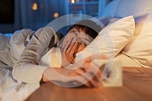 sleepy asian woman with clock in bed at night