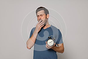 Sleepy bearded man with alarm clock on grey background