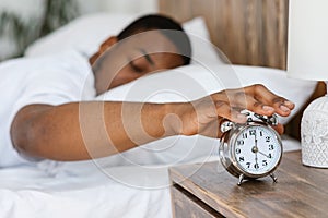 Sleepy Black Man Turning Off Alarm Clock Lying In Bed