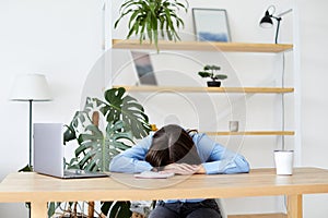 Sleepy bored woman office worker lying on table with laptop, feeling lack of energy sitting at workplace