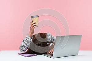 Sleepy bored woman office worker lying on table with laptop holding and showing paper coffee cup, feeling lack of energy sitting