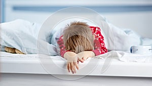 Sleepy boy lying in bed with blue beddings. Tired child in bedroom