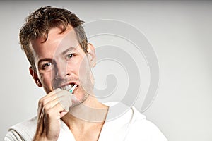 Sleepy caucasian guy brushing tooth wearing bathrobe, in the morning