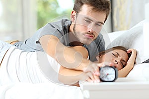 Sleepy couple waking up turning off alarm clock in the bed