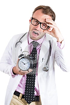 Sleepy, exhausted male doctor wearing glasses holding an alarm clock, tired after a busy da