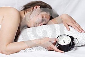 Sleepy girl can not wake up from the alarm bell. A woman is sleeping in bed and holding an alarm clock in her hand