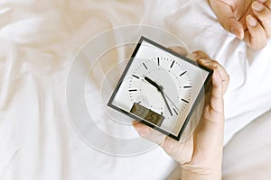 Sleepy girl`s hand showing alarm clock and waking up late in the morning.