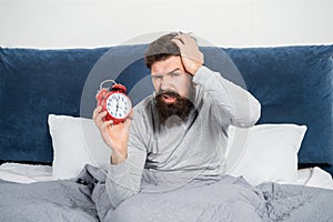 Sleepy guy holding alarm clock being in bed in morning, oversleep