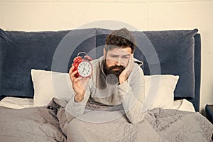 Sleepy guy holding alarm clock being in bed in morning, time