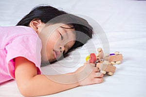 Sleepy kid on white bed, playing number wooden toy. Asian child lying down on mattress. Dry skin under the eyes.