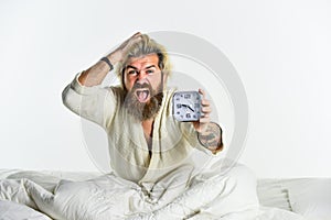 Sleepy mad guy and alarm clock in bed. Bearded man with alarm clock. Sleep disorder. Awakening concept. Sleep is