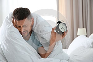 Sleepy man with alarm clock at home