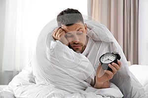 Sleepy man with alarm clock at home